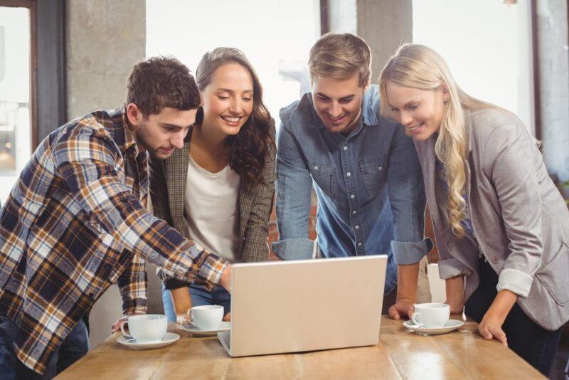 Smiling friends standing and pointing on laptop screen